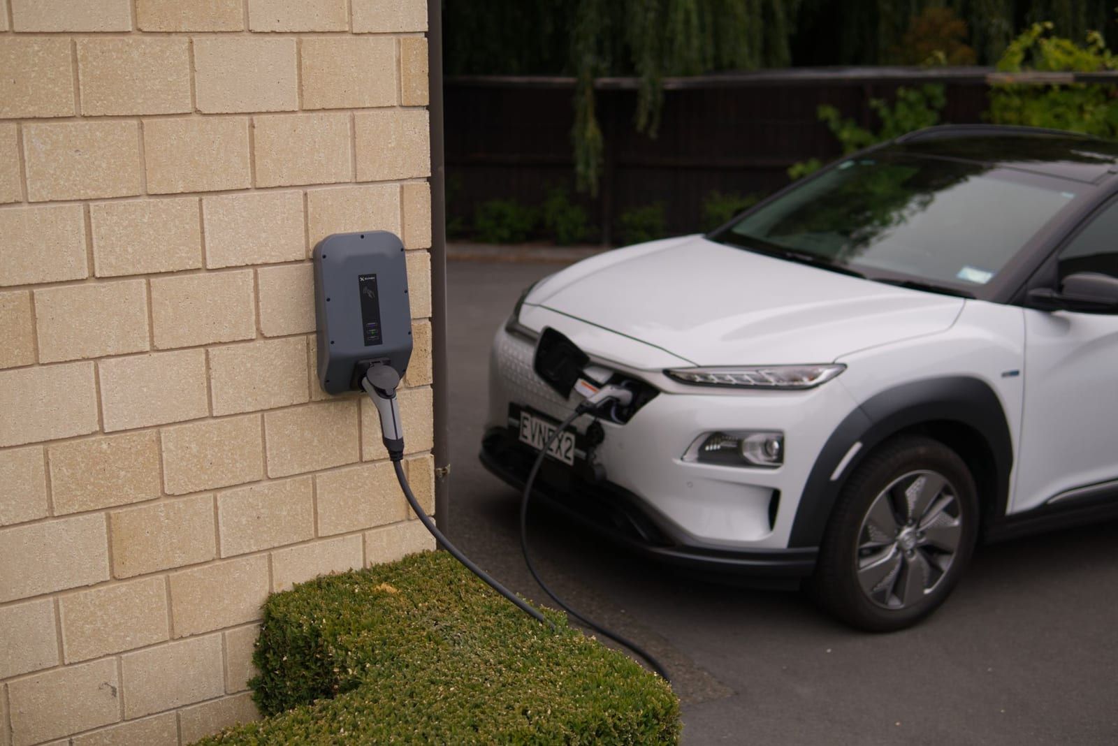 An electric car charging from a home charger on a driveway