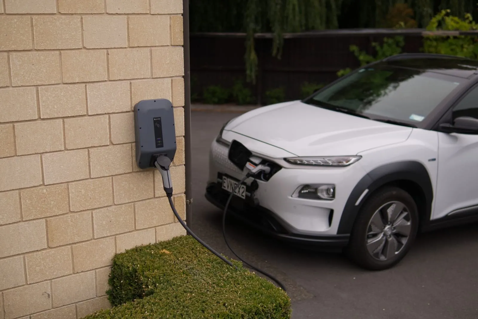 An electric car charging from a home charger on a driveway